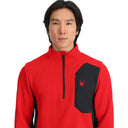 Person wearing a red and black pullover with a spider logo on a white background